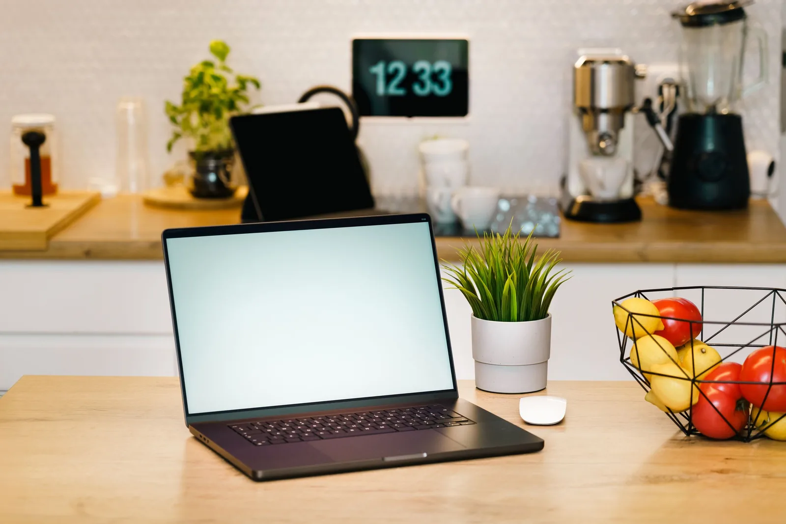 Laptop auf einem Küchentisch, daneben ein Obstkorb, dahinter eine Kaffeemaschine