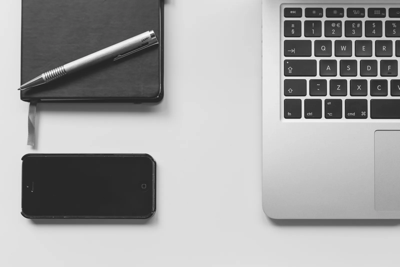 Laptop, Smartphone und Notizbuch mit Stift auf einem hellen Schreibtisch