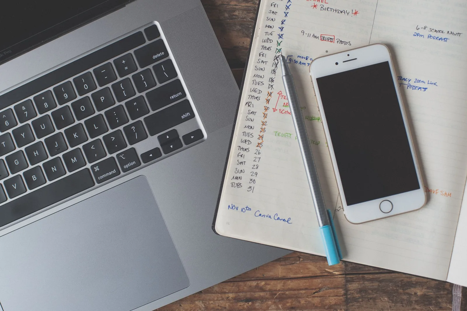 Laptop, Smartphone und handschriftlicher Planer auf einem Holztisch