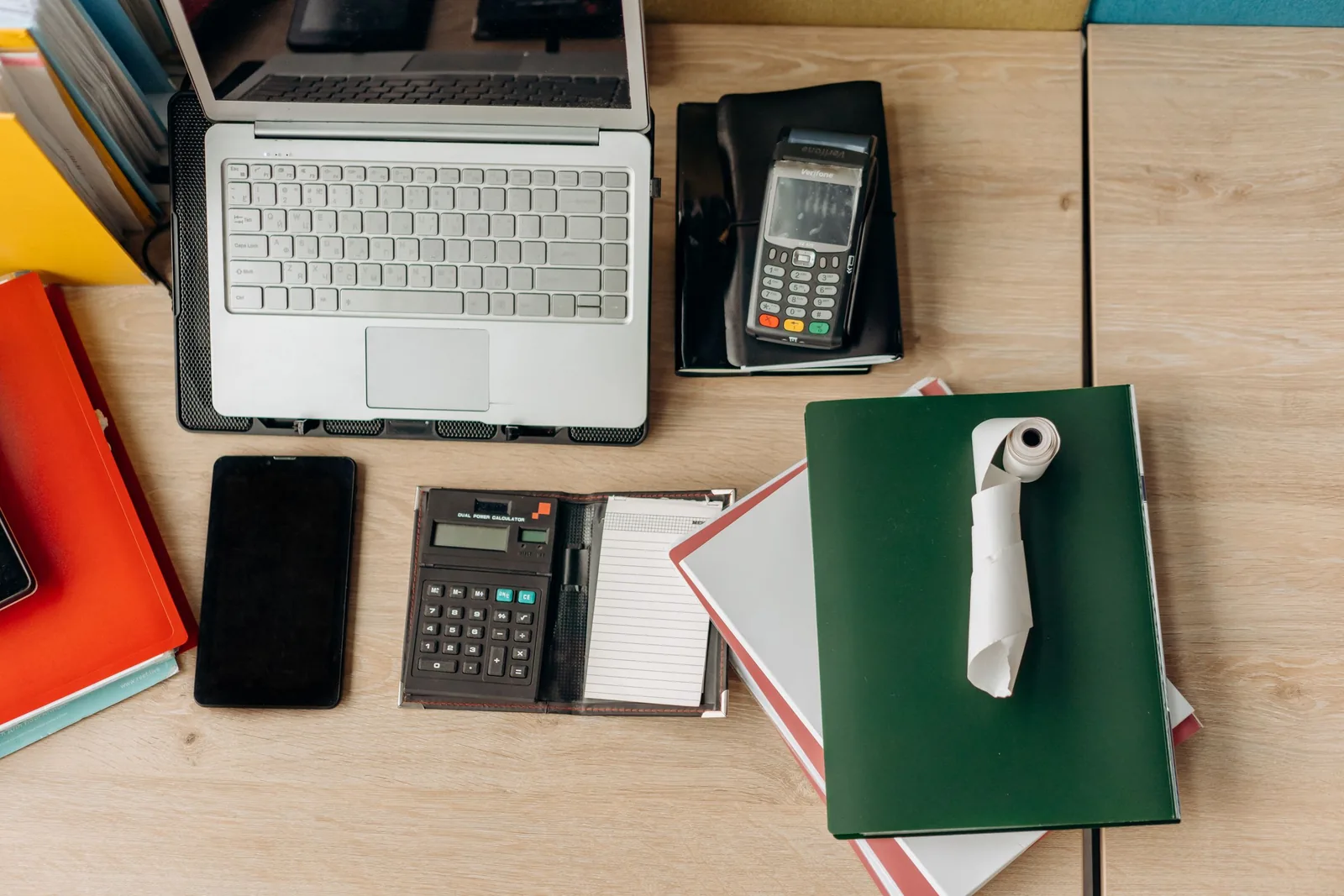 Schreibtisch von oben mit Laptop, Kartenterminal, Taschenrechner und Mappen