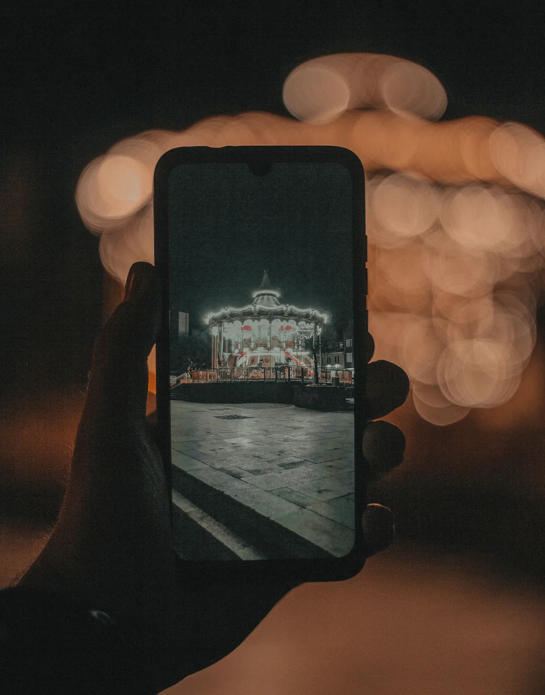 Smartphone fotografiert bei Nacht ein beleuchtetes Karussell